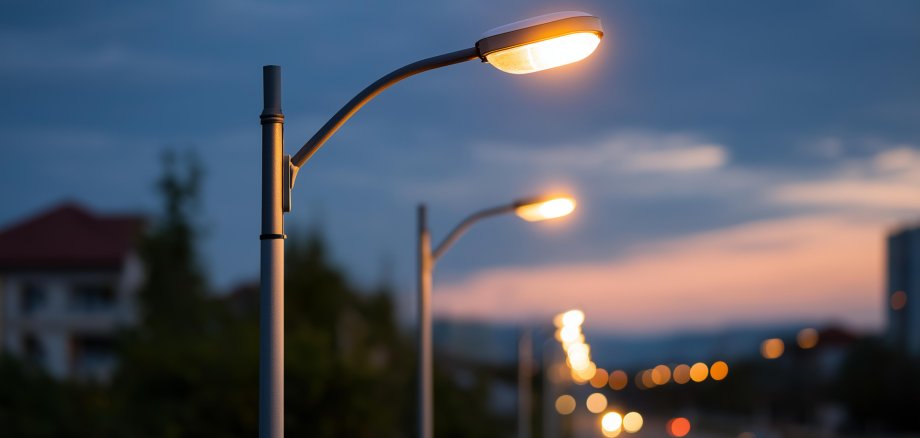 Modern LED street lighting poles illuminating urban area at twilight city infrastructure public lighting municipal services energy efficient streetlights urban Beispielbild AdobeStock