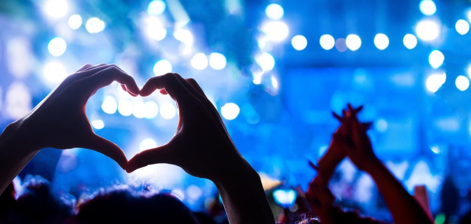 Crowd of Audience at during a concert with silhouette of a heart shaped hands shadow, light illuminated is power of music concert